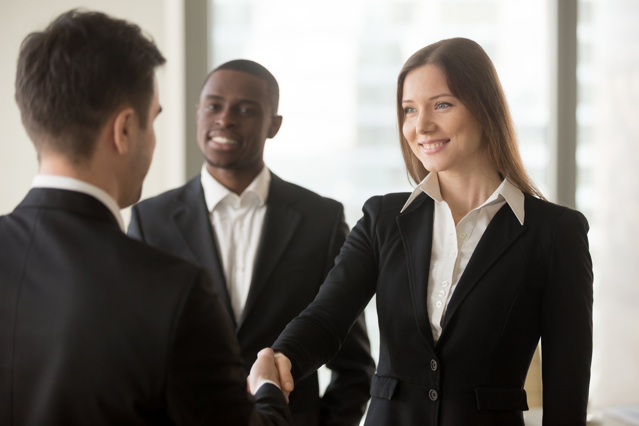 Female professional shaking hands with male professional while a second male professional looks on