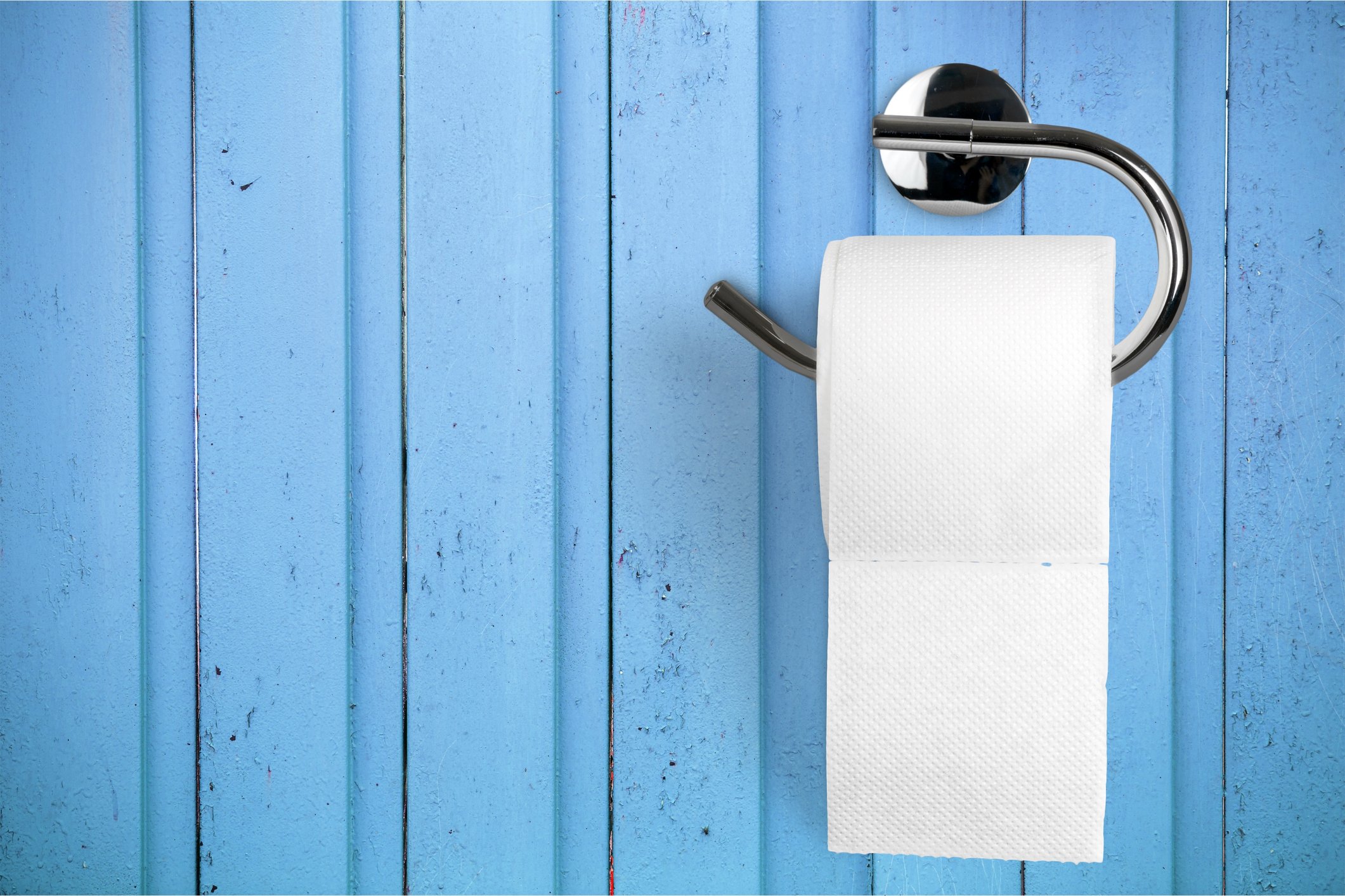 Toilet paper on holder attached to a light blue wall. 