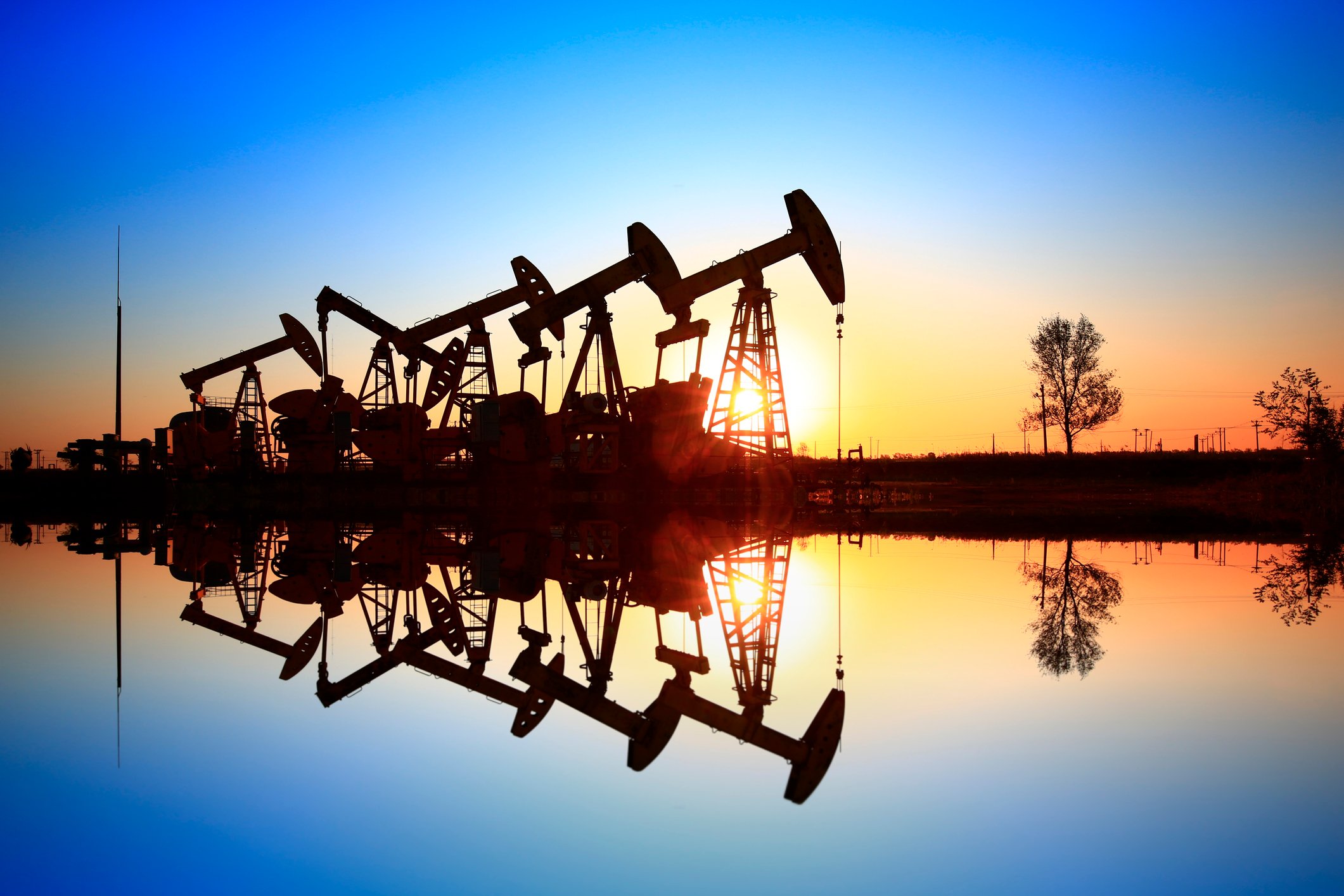 A row of oil pumps reflected on a lake at sunset