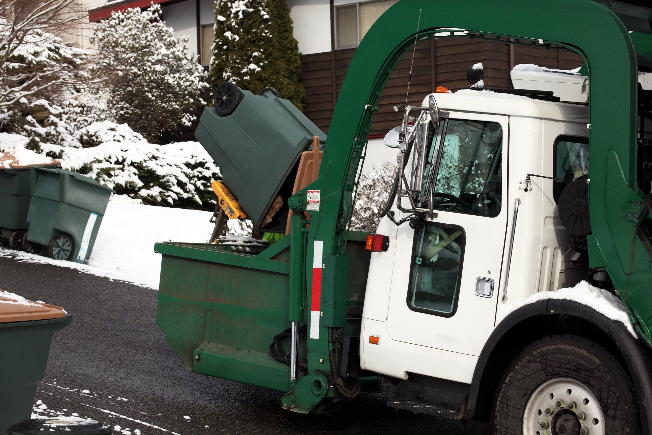 A garbage truck picking up trash in the snow.