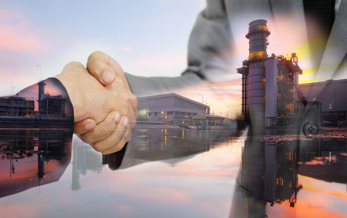 Two people shaking hands superimposed over an electricity-generating facility.