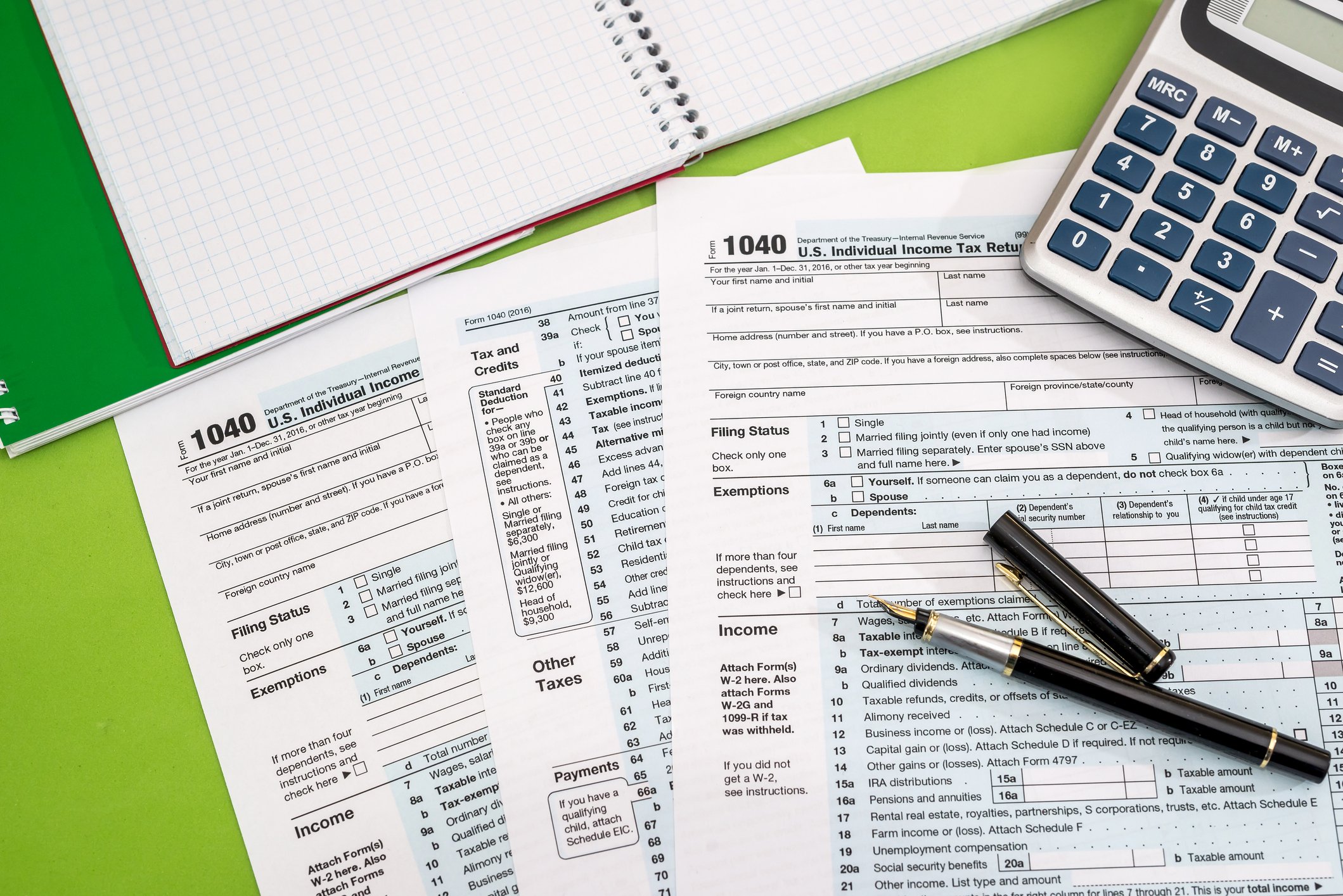 1040 tax forms with a calculator, an open graph notebook, and black fountain pen on a green background.