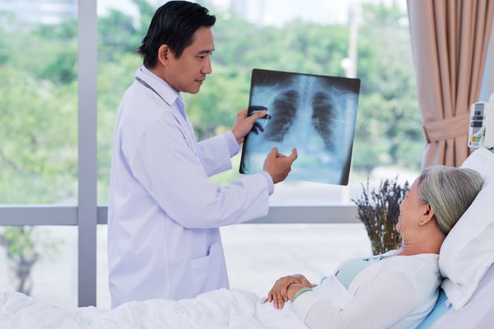 A doctor showing a patient her chest X-ray while she's lying in a hospital bed.
