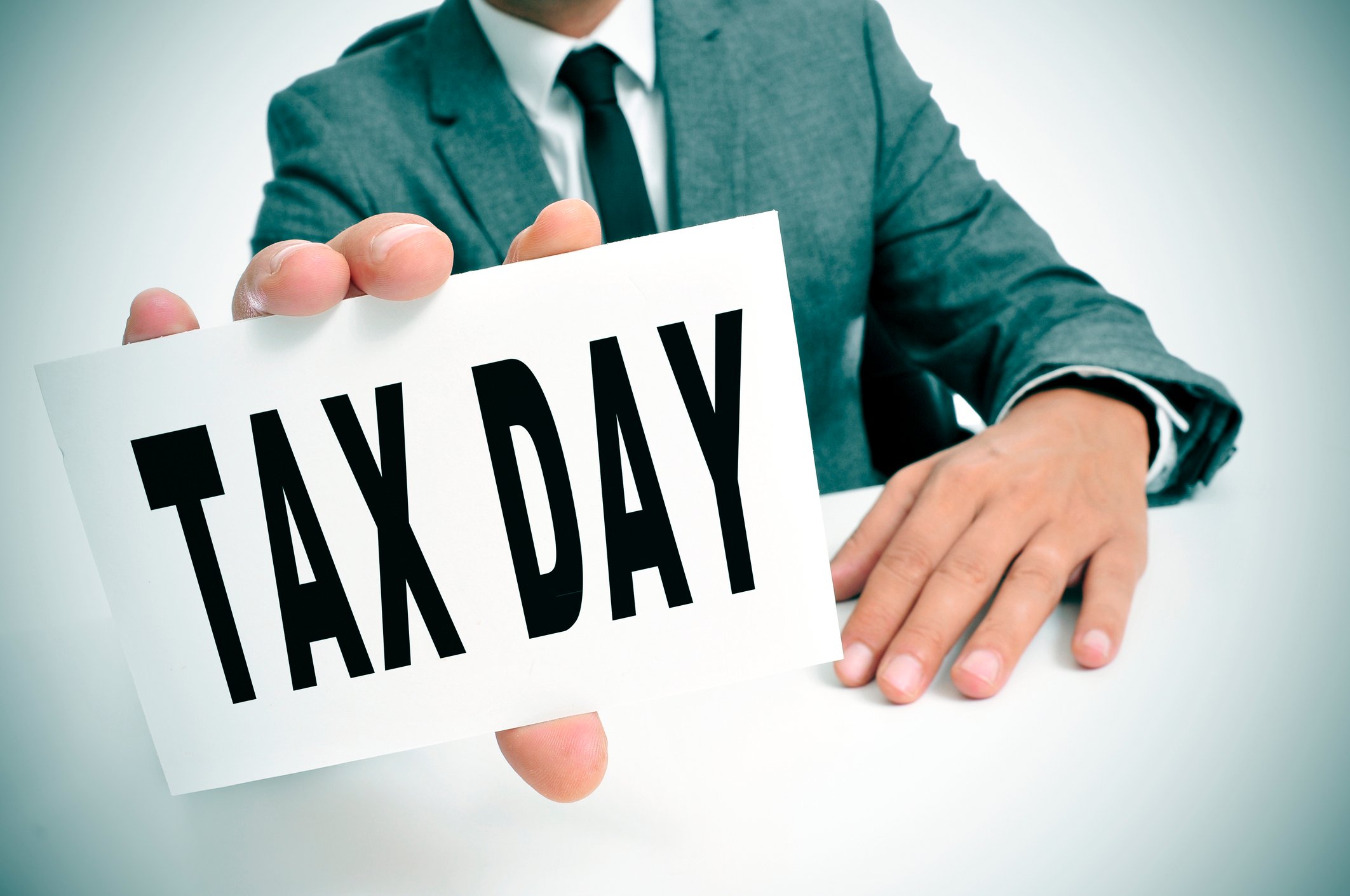 A man in a suit holding up a sign that reads, Tax Day.
