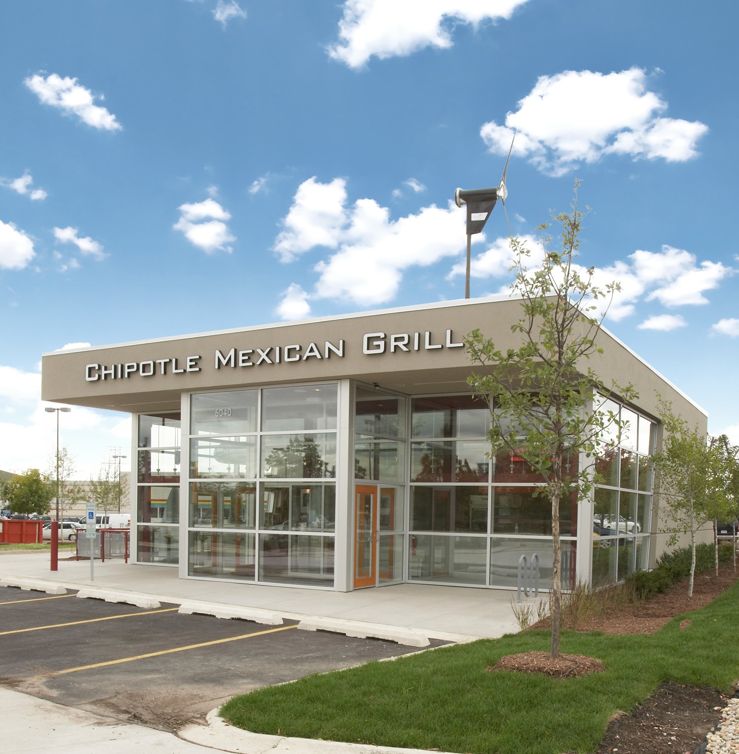 An all-glass Chipotle restaurant on a sunny day with blue skies and puffy white clouds.