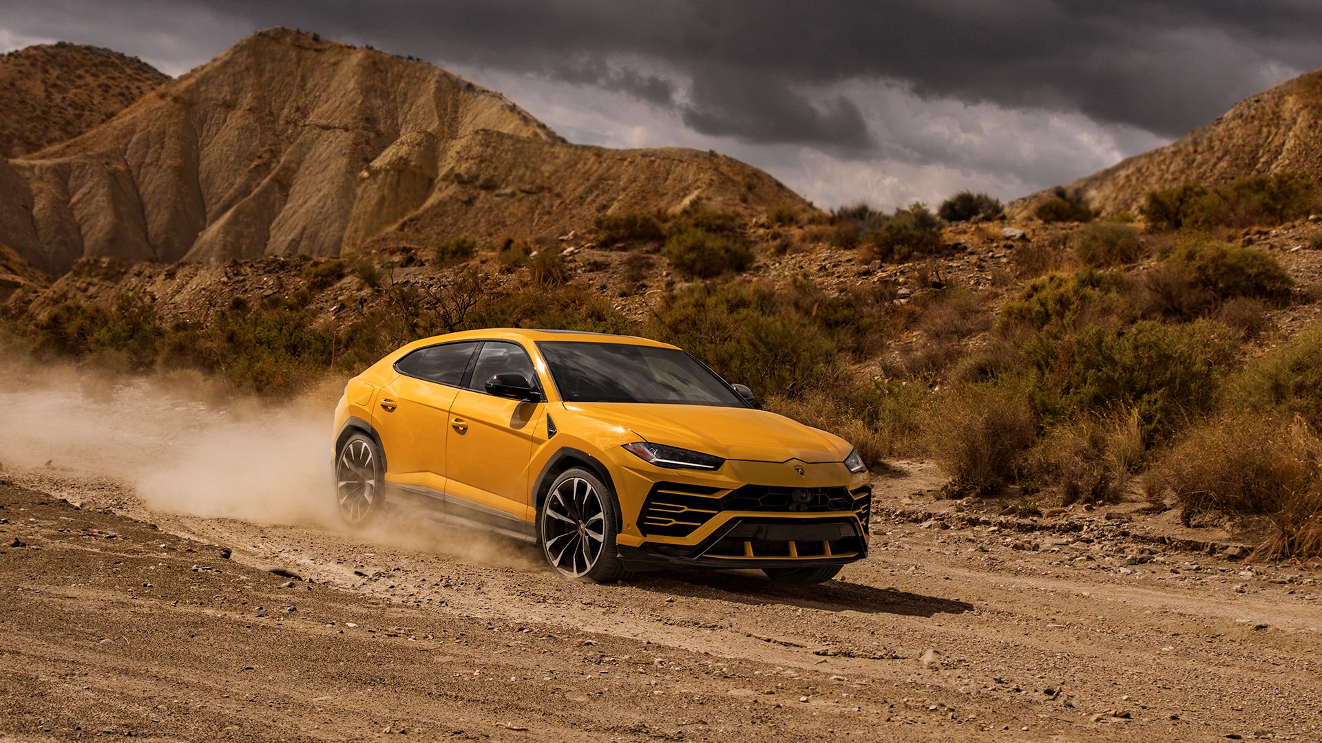 A yellow Lamborghini Urus driving offroad in a desert.
