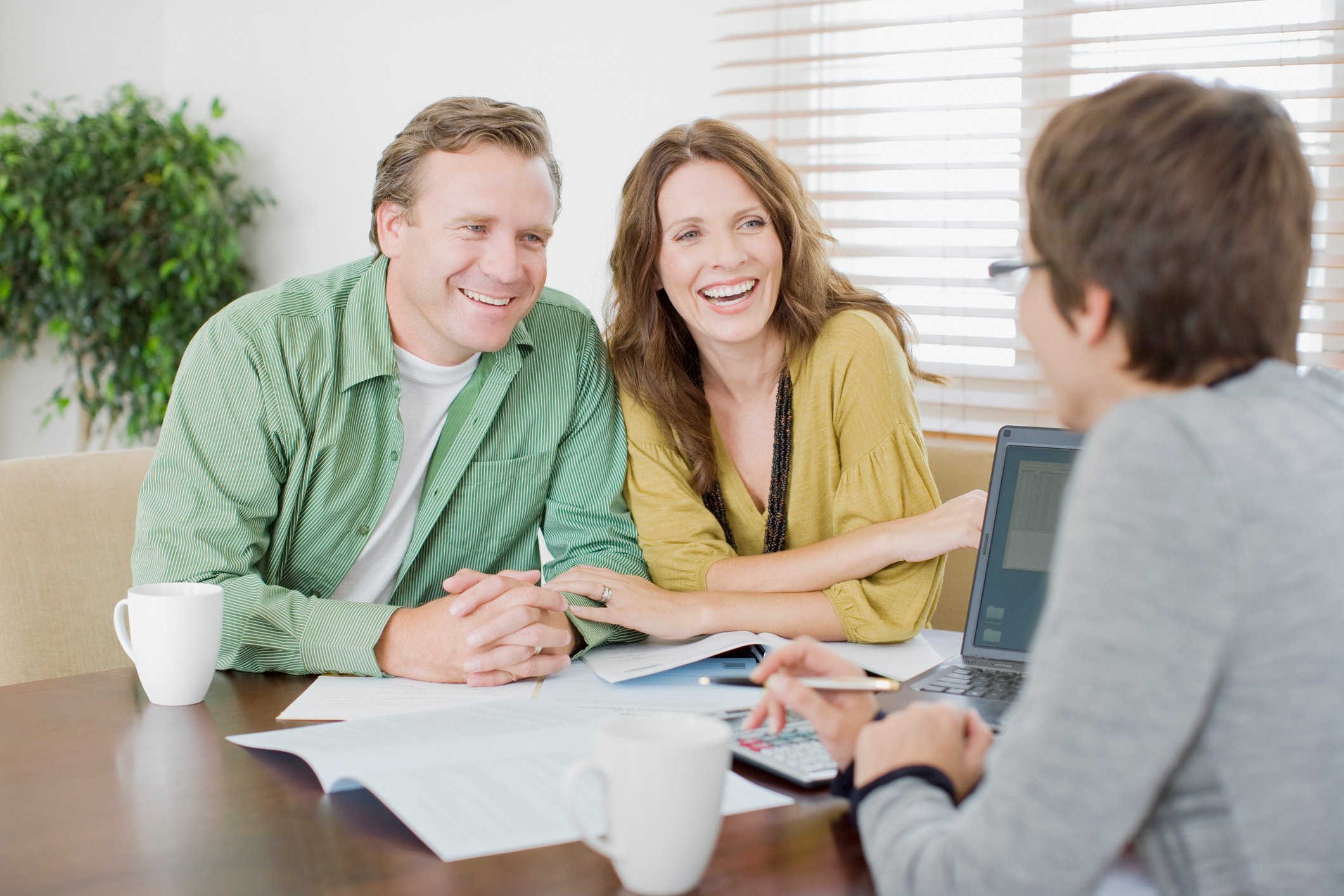 A smiling couple meets with a person on the other side of the desk, in an office setting.