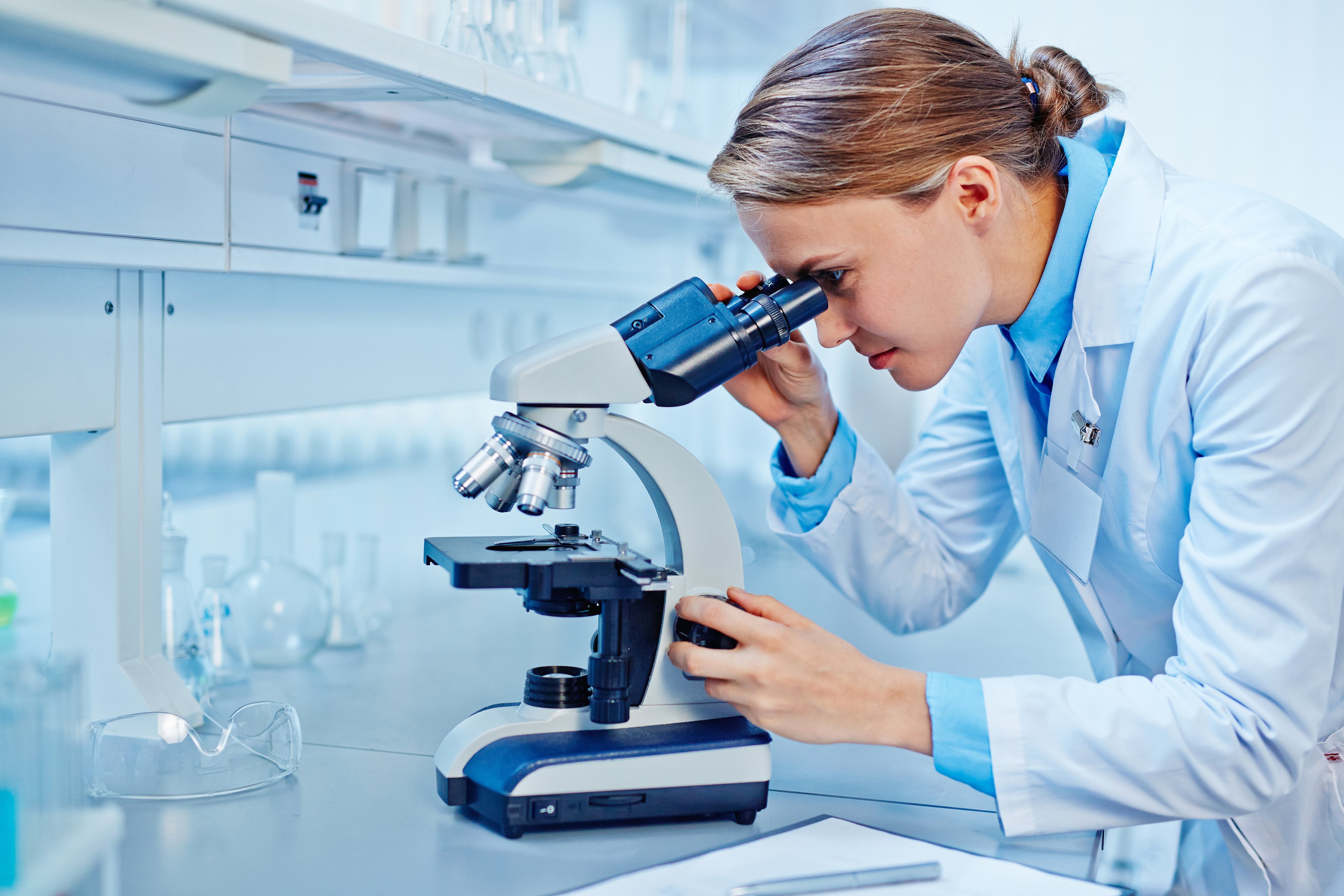 Woman in lab coat looking through a microscope