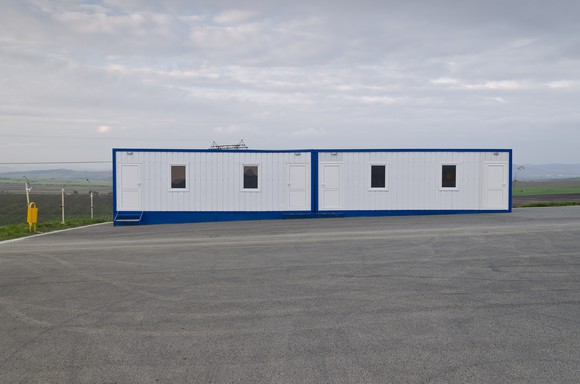 Modular building with four windows in a parking lot. 