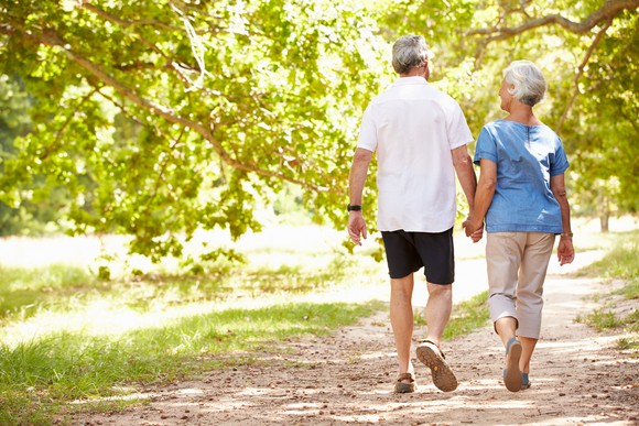 Man and woman in their 60s walking down a path holding hands.
