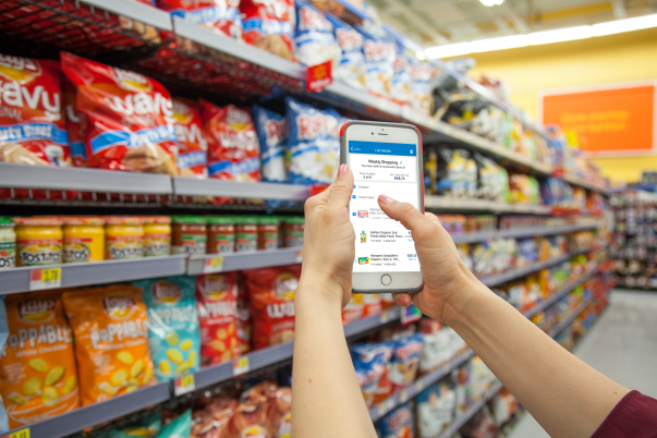 A person uses the new Wal-Mart app in a store, holding their phone up in front of racks of food for sale..