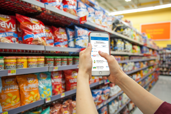 A person uses the new Wal-Mart app in a store, holding their phone up in front of racks of food for sale..