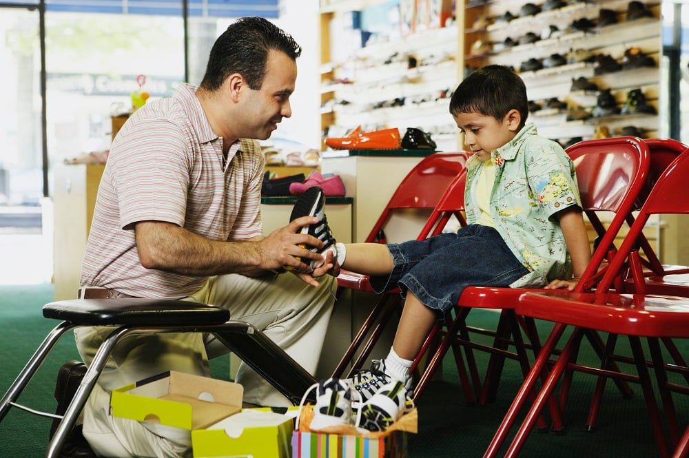 A man helps a young boy try on a pair of shoes in a shoe store.