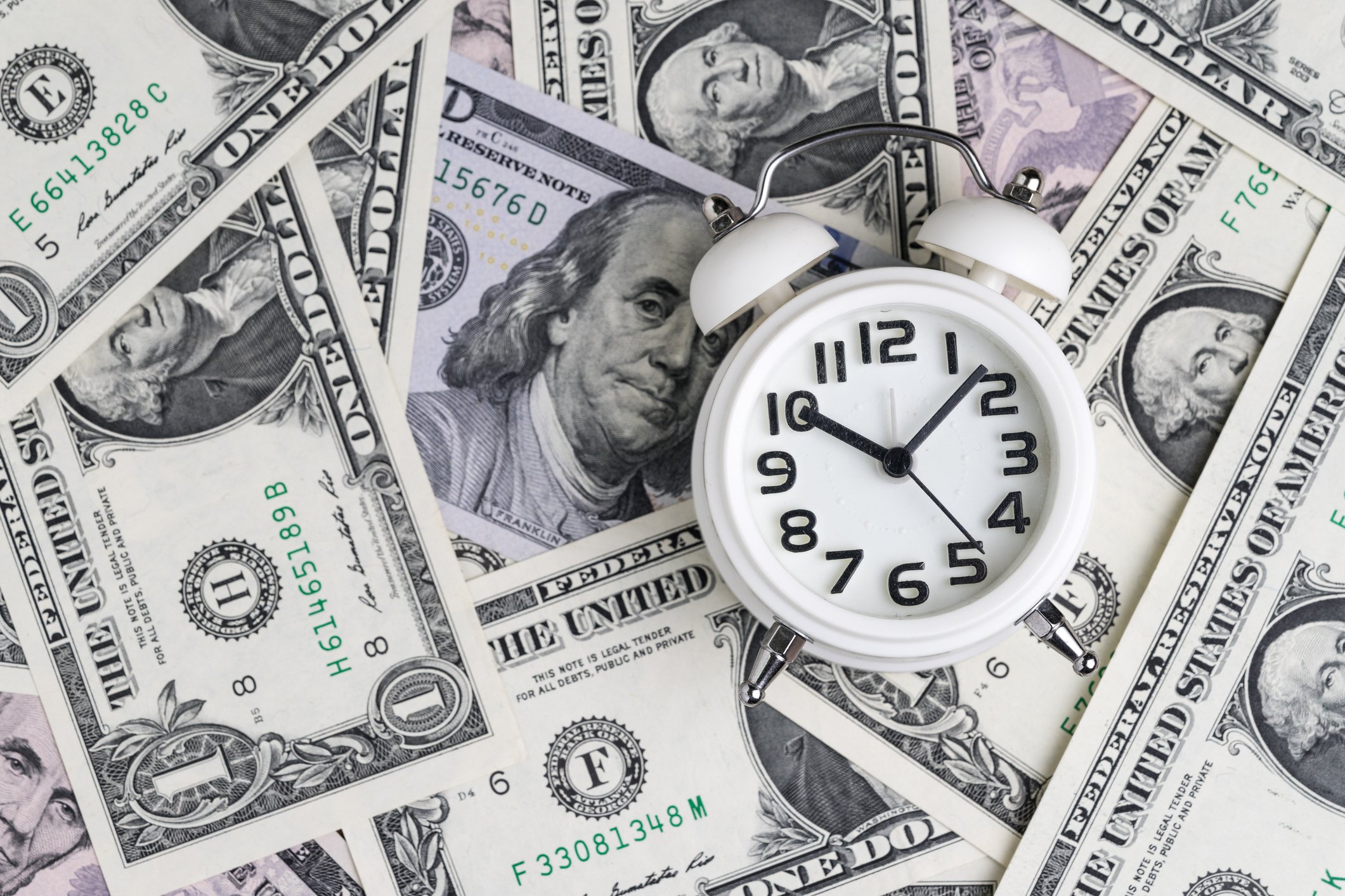 Alarm clock on pile of dollar bills