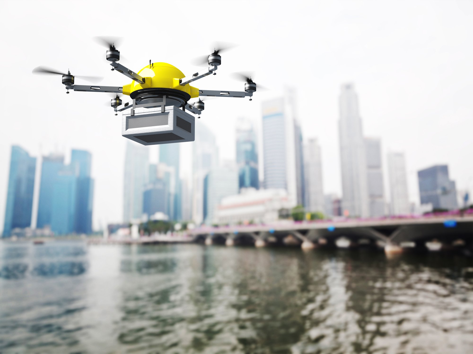 A package-carrying drone flying over a body of water and toward a city.