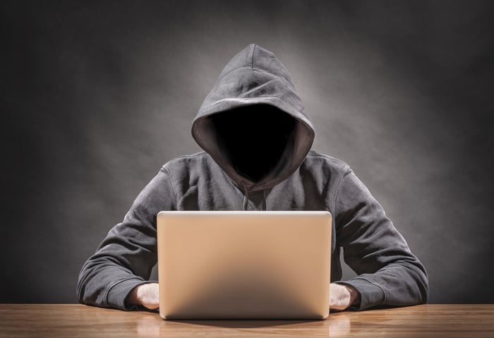 Hacker in a hoodie sitting with a laptop.