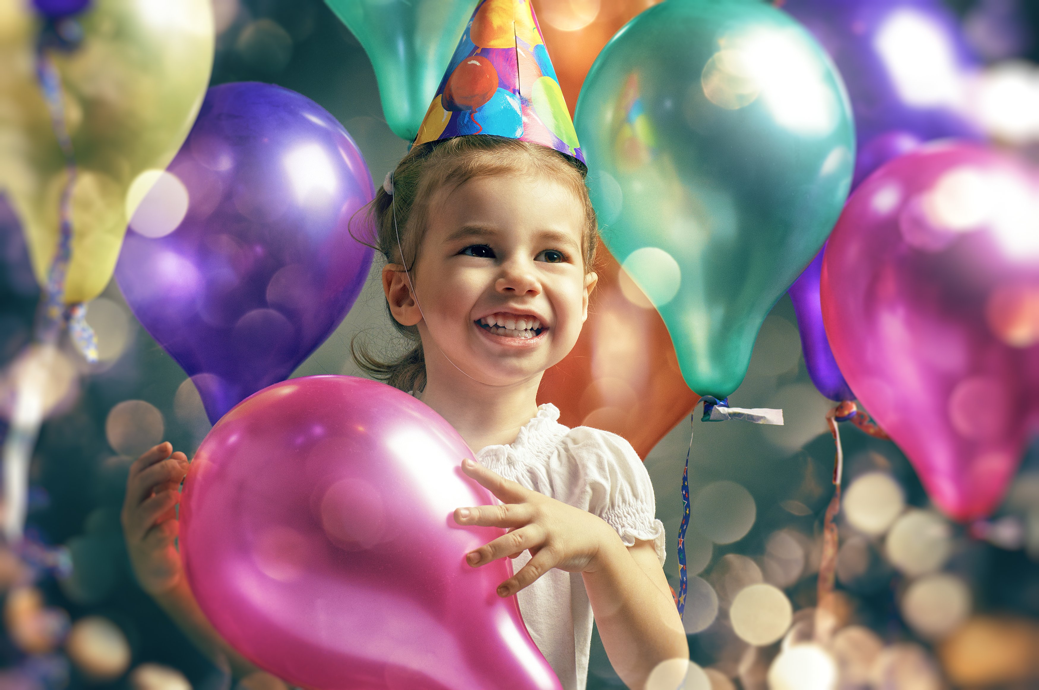 Young girl holding a pink balloon while surrounded by balloons in other colors