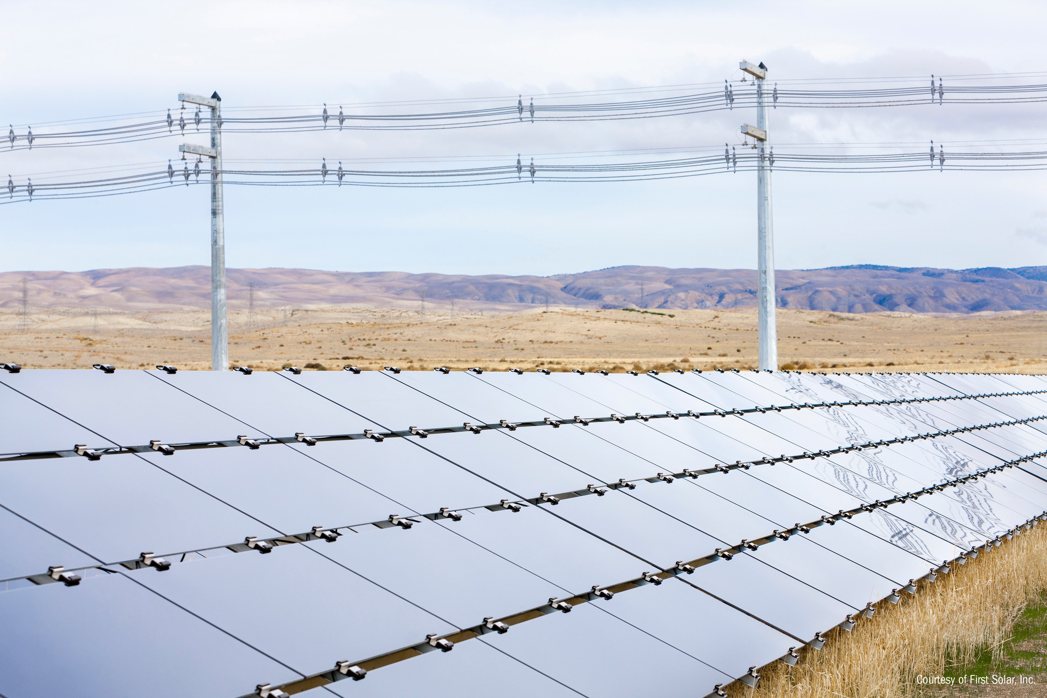 Solar array in front of power lines in a field. 