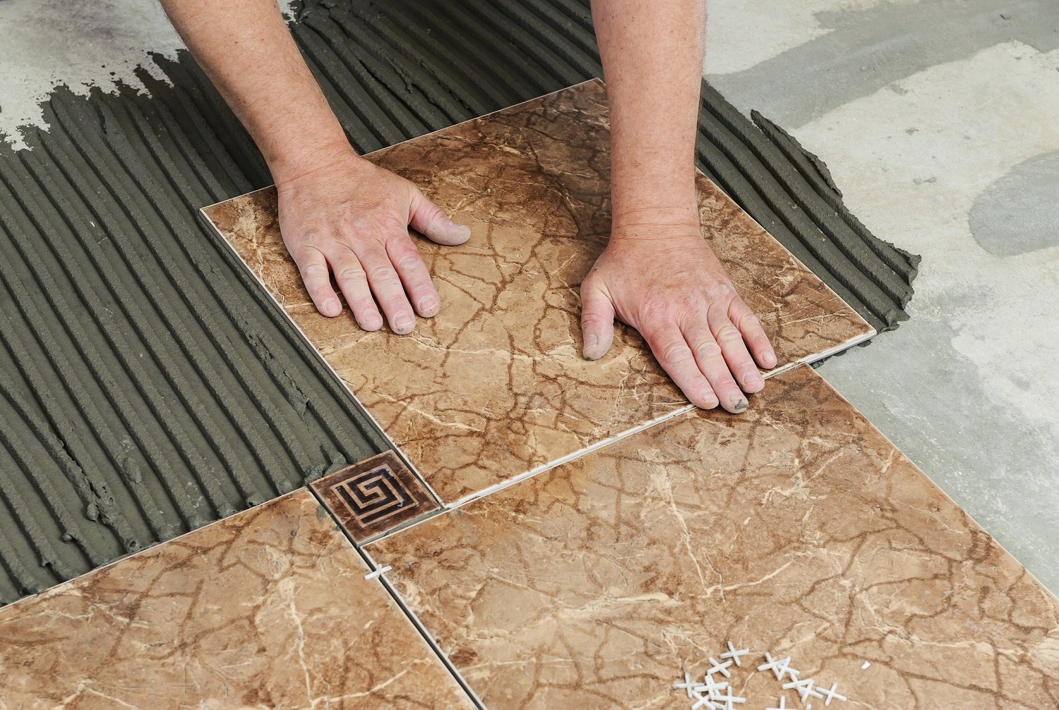 A worker laying brown tile on a floor.