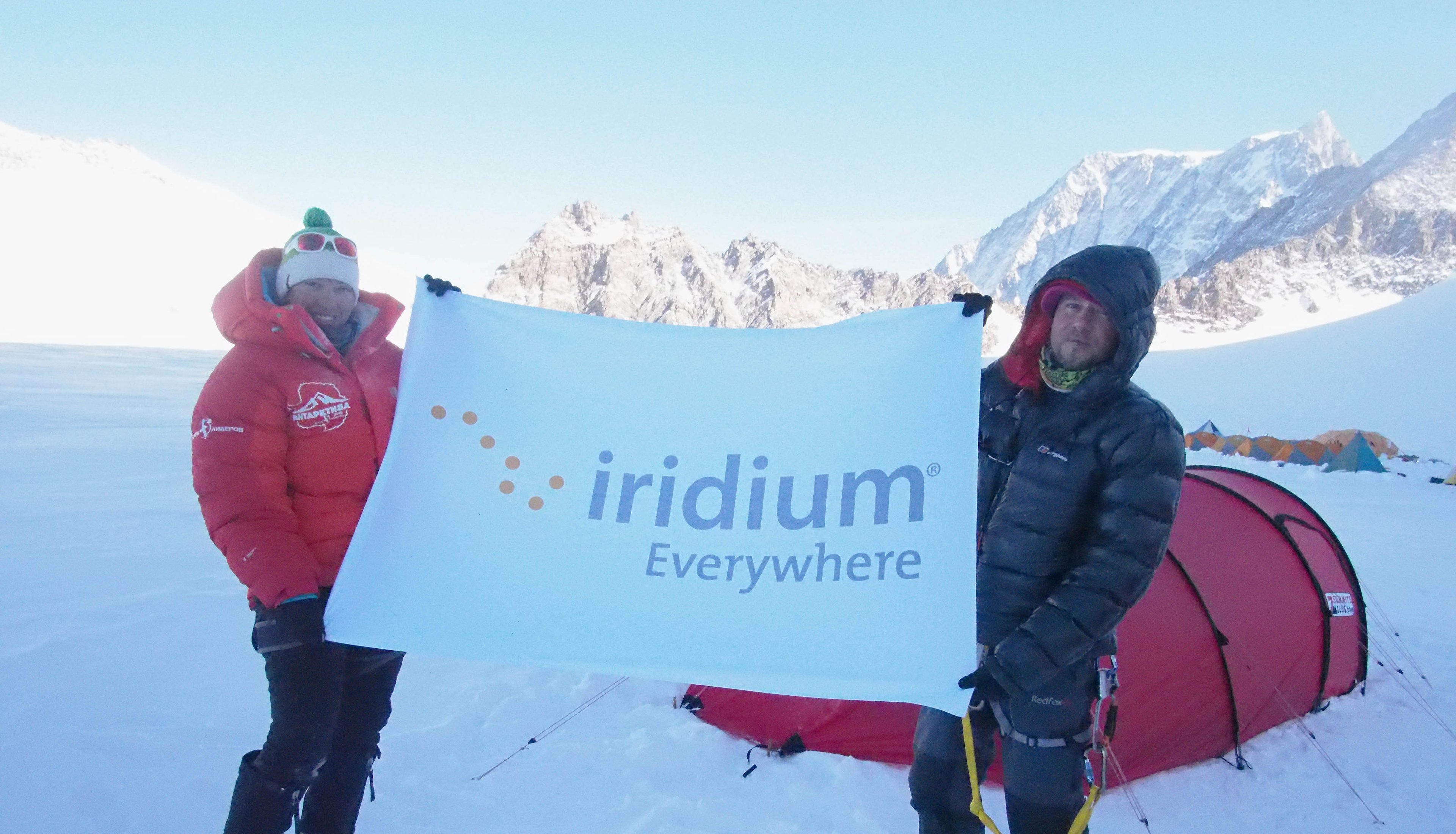 Two people in a winter setting holding a sign saying Iridium Everywhere.