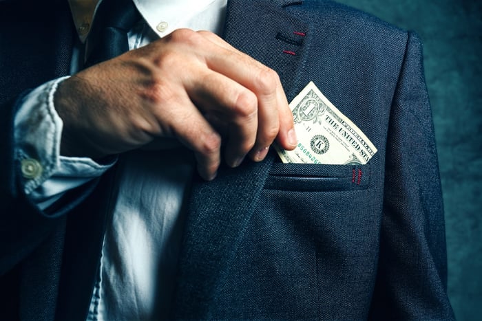 Man putting $1 bill into suit pocket