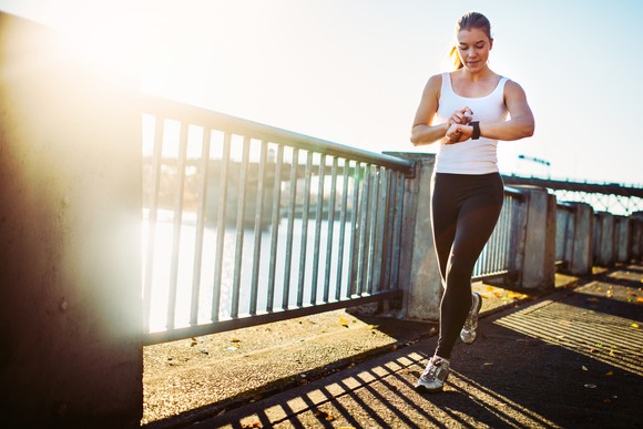 A jogger tapping a smartwatch while running.
