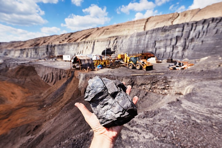 A hand holding up a piece of coal in an open pit mine.