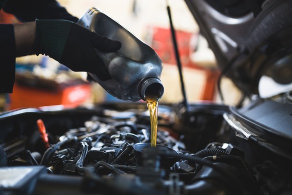 Oil being poured into a vehicle by hands in black gloves.