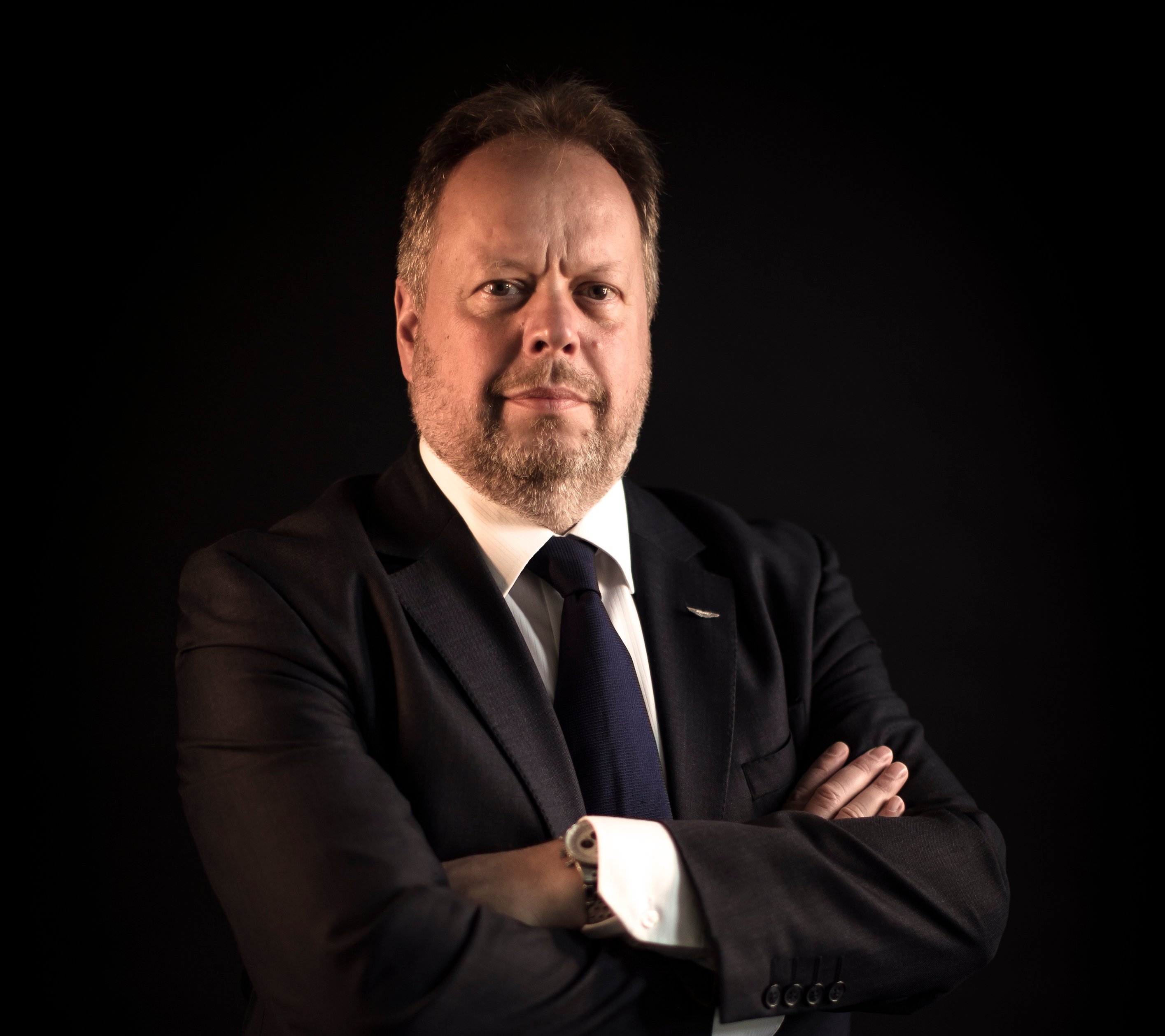 Palmer is standing, arms crossed, before a dark backdrop.