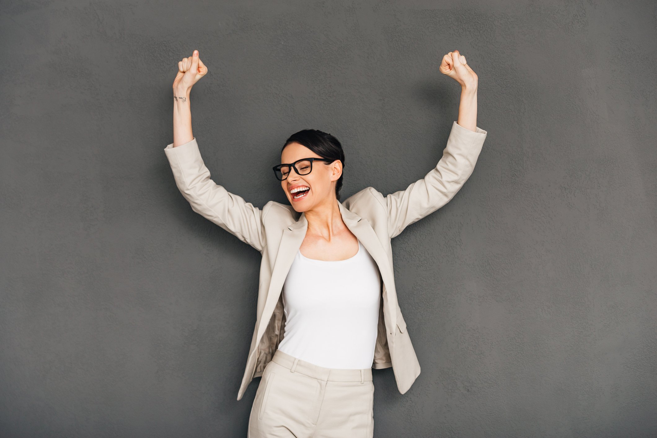 Bespectacled woman in business suit raising her arms in celebration