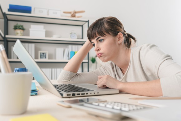 Woman looking at laptop with bored expression.