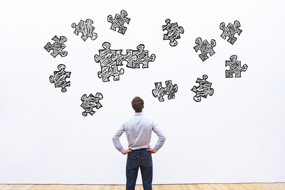 Man in white shirt and blue slacks watching a wall mural of several puzzle pieces, only some of which are fitting together.