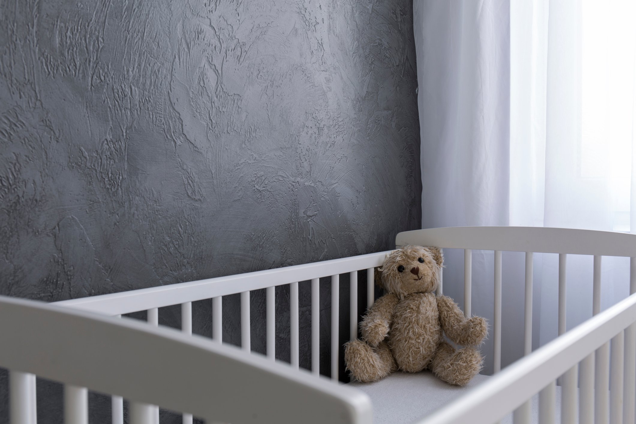 Stuffed bear sitting in the corner of a baby crib.