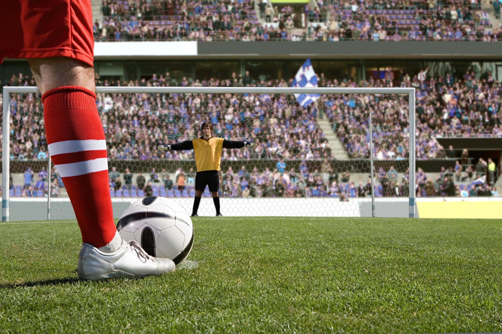 A soccer player lines up a penalty kick. We view the goalie from behind the ball.