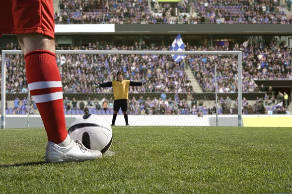 A soccer player lines up a penalty kick. We view the goalie from behind the ball.