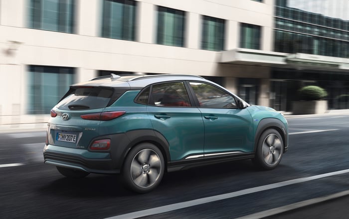 A rear three-quarter view of the Kona Electric as it drives on a city street. 