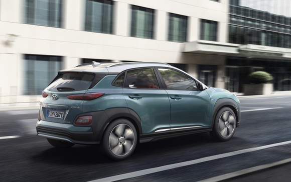 A rear three-quarter view of the Kona Electric as it drives on a city street. 