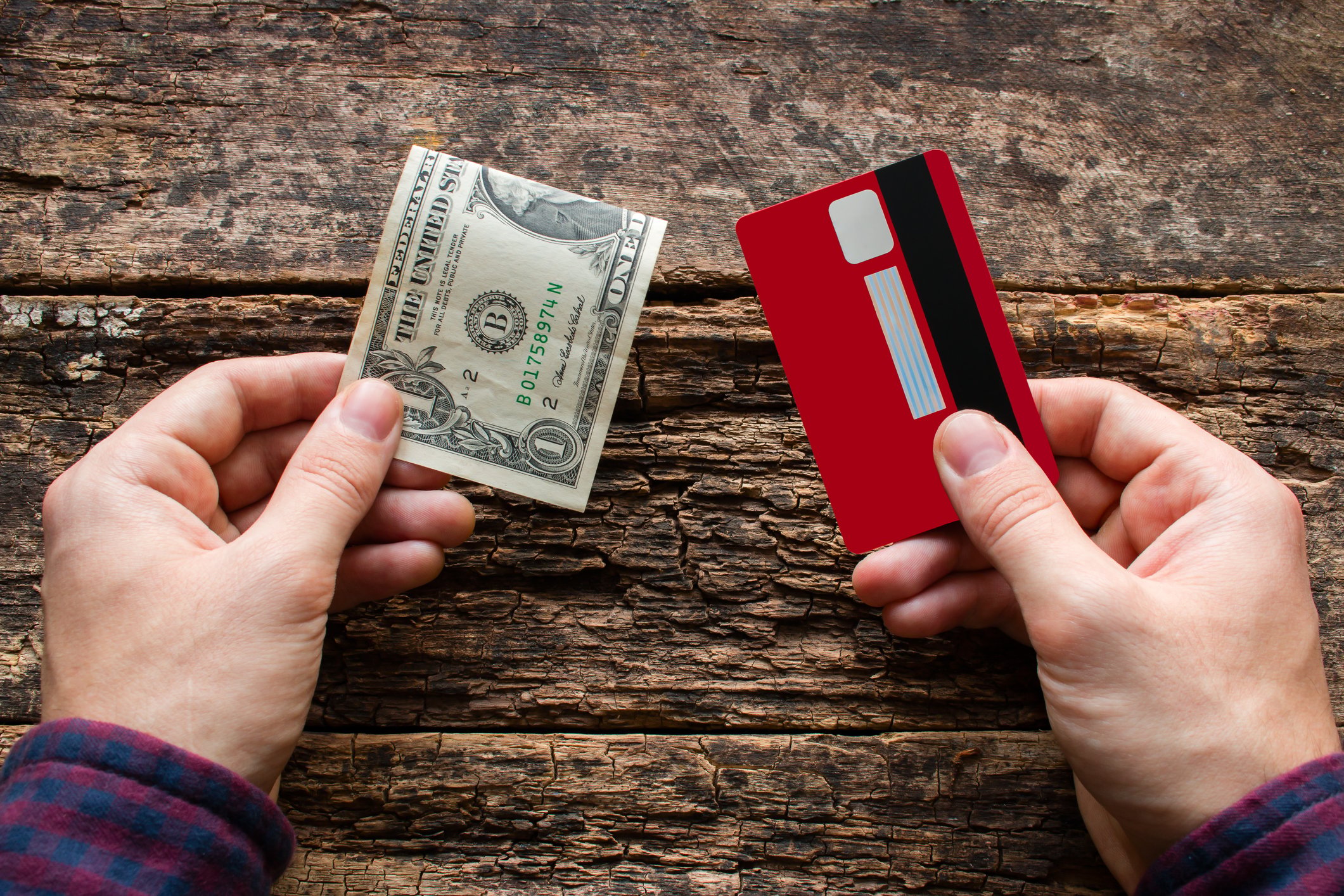 A person holding a dollar bill in one hand and a credit card in another.
