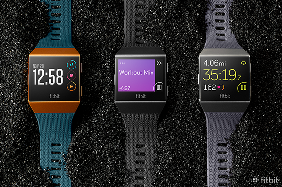 Three Fitbit Ionic smartwatches in a row on a black-and-white speckled surface
