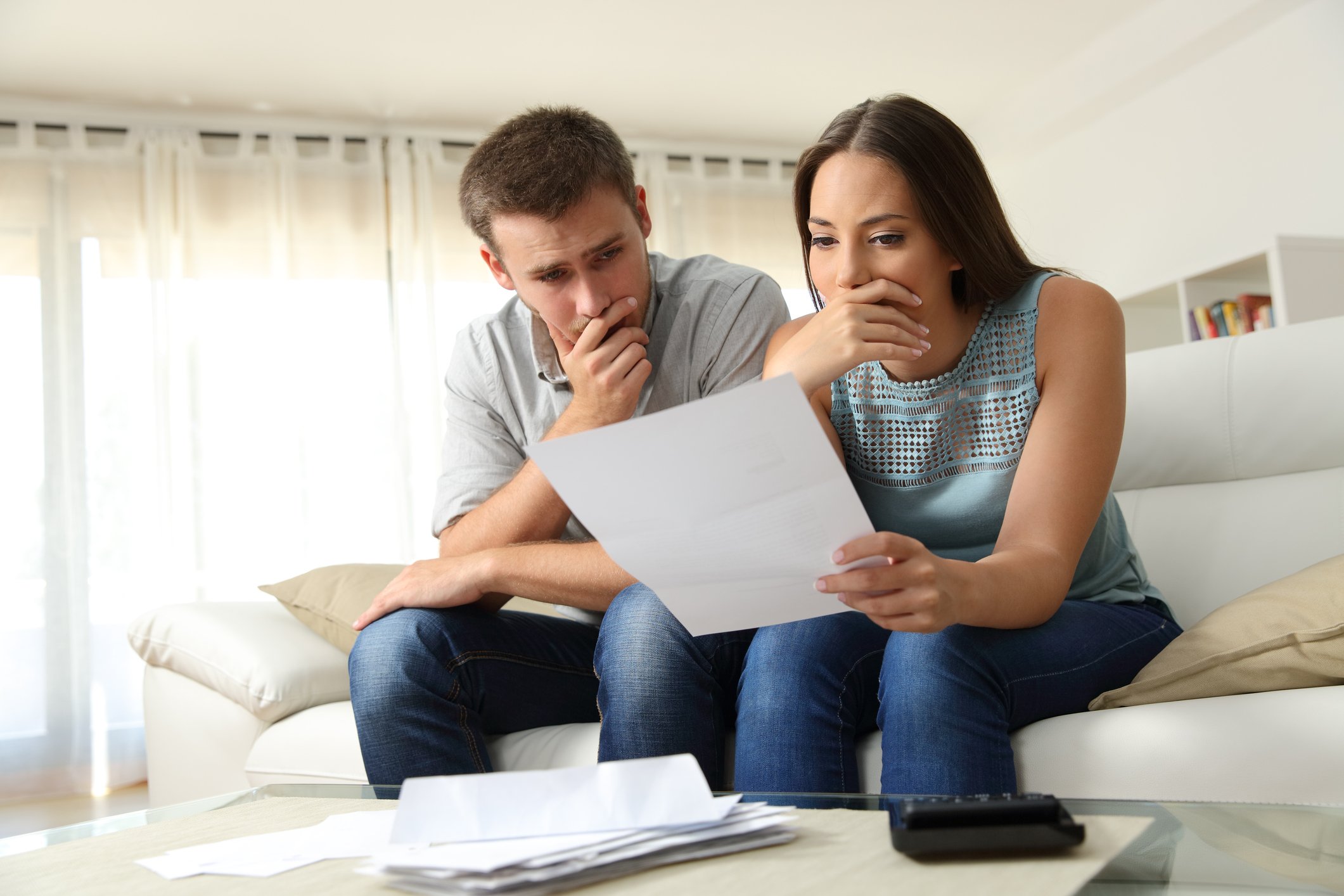 A young couple sitting on a couch and looking at a bank statement.
