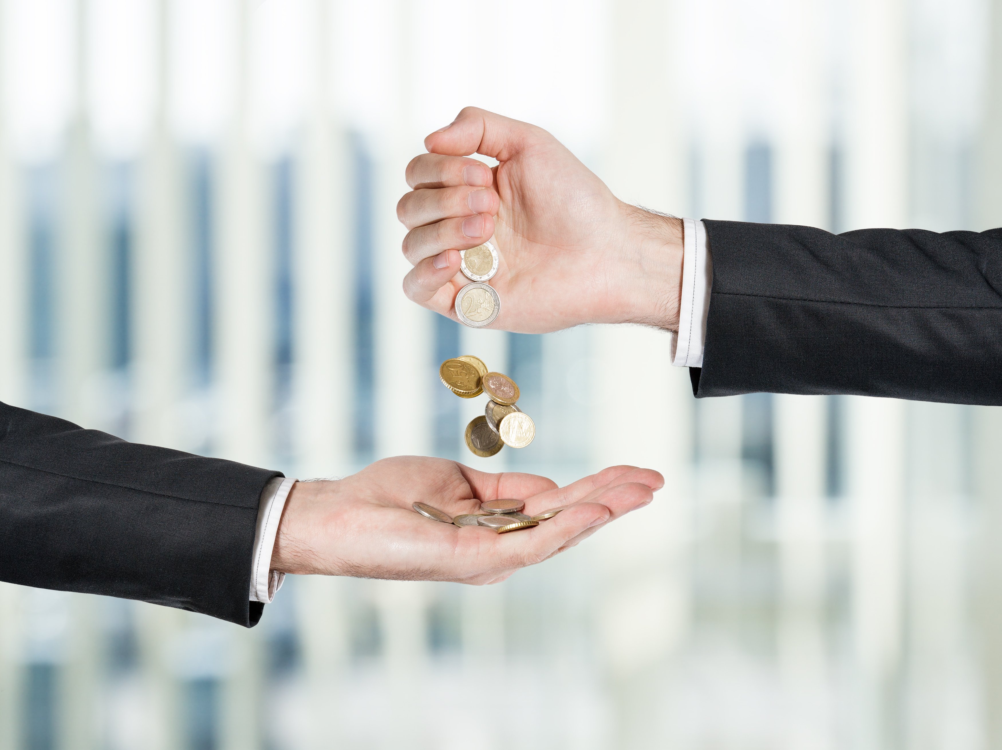One hand pouring coins into someone else's hand.