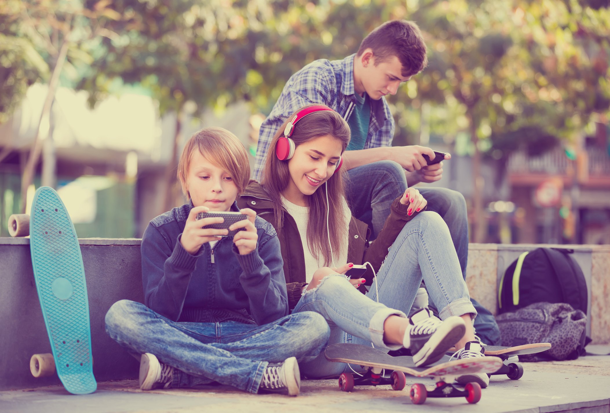 Three teenagers sitting outside, using smartphones.