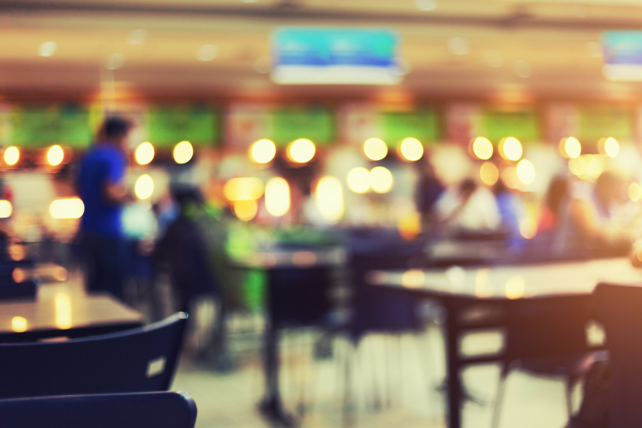 A blurry quick-service restaurant with many customers seated at tables