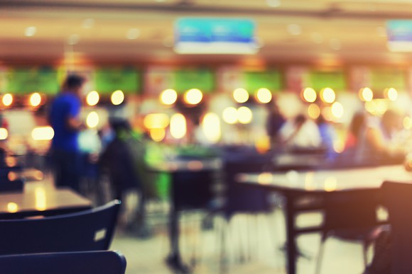 A blurry quick-service restaurant with many customers seated at tables