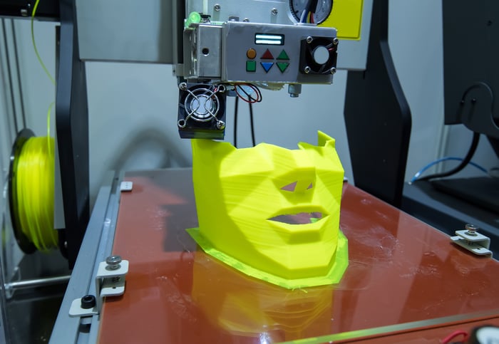 A 3D printer printing a yellow plastic human mask or face.