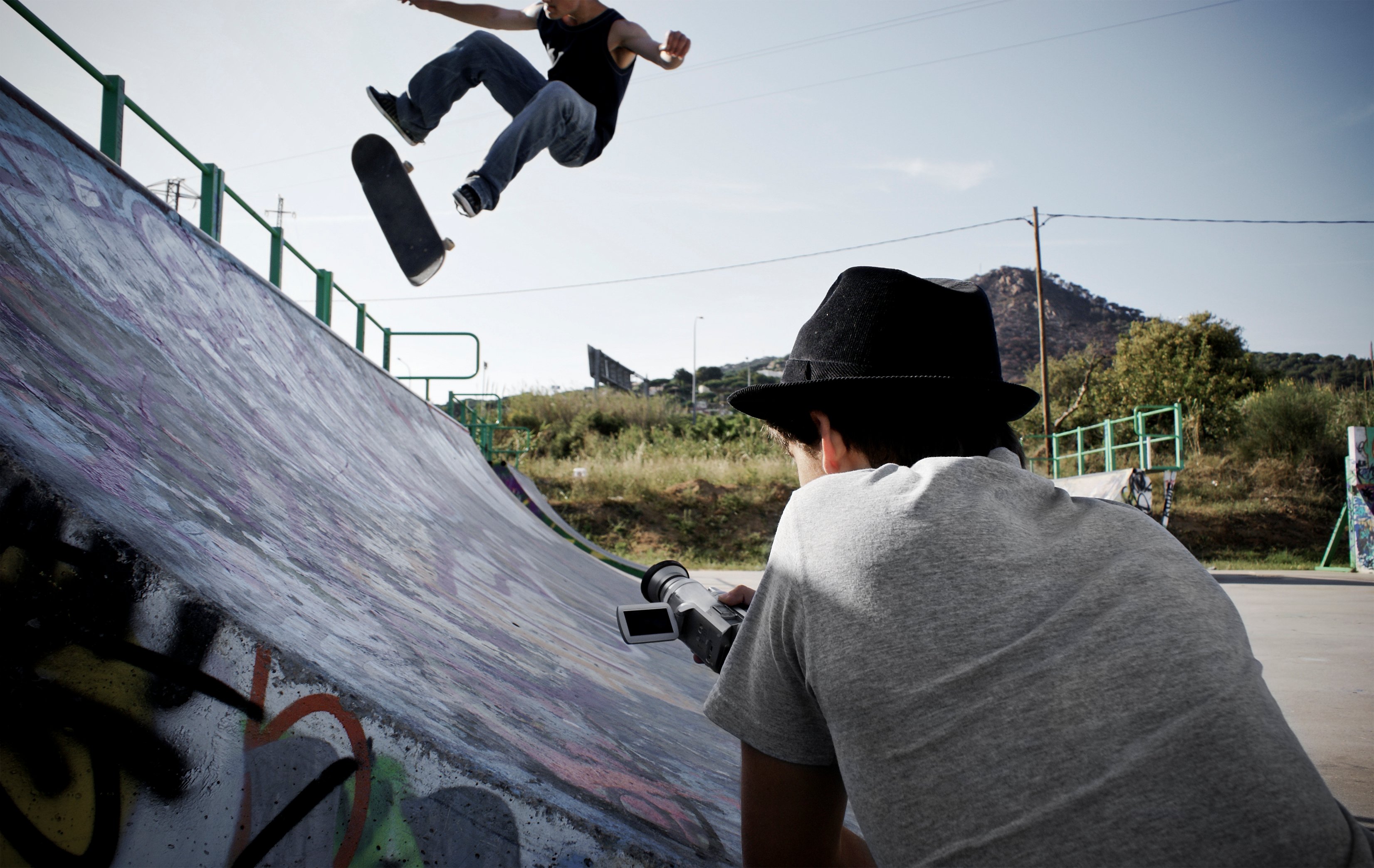 A person filming a skateboarder who is in the air doing a trick.