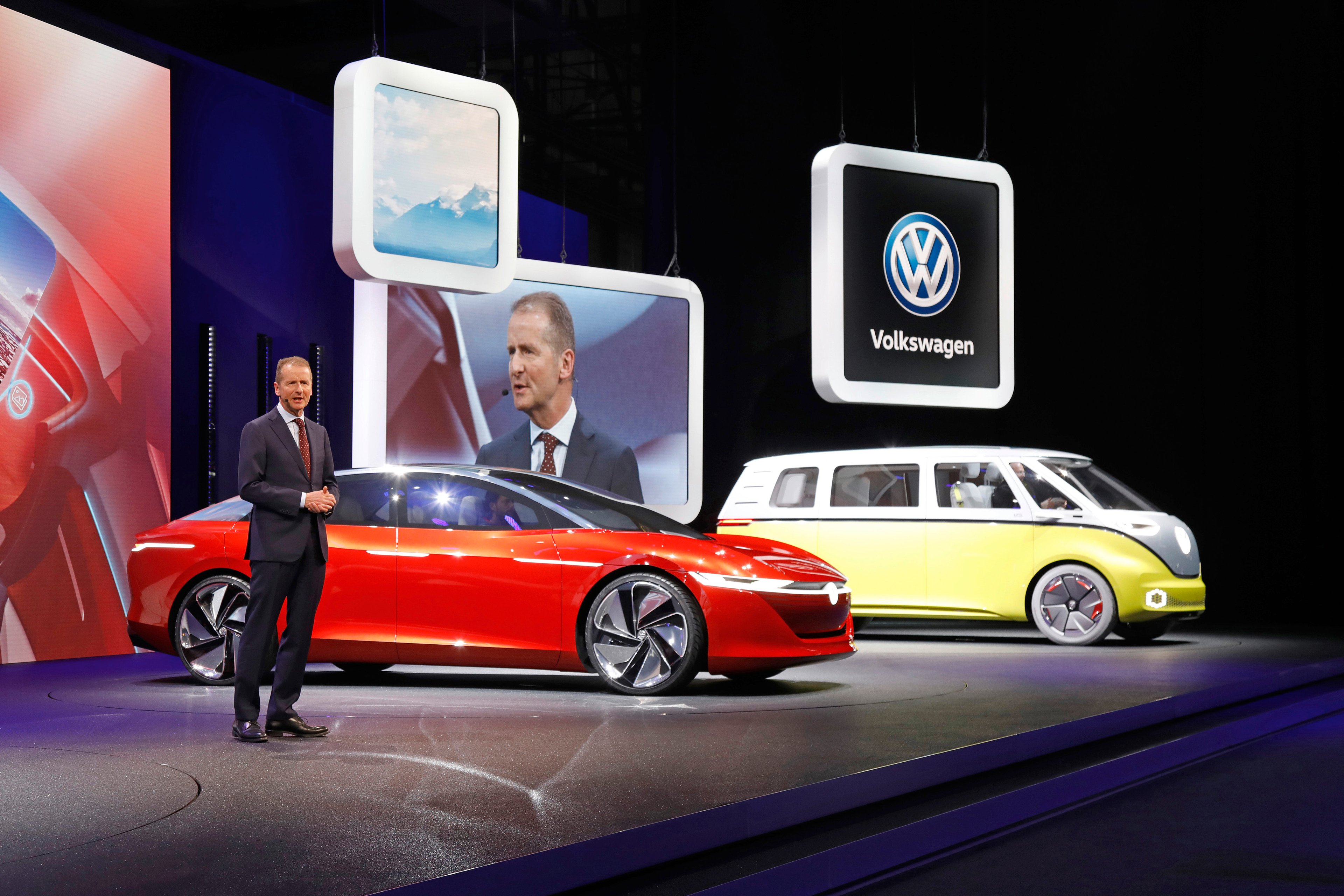 Diess is speaking on stage next to the I.D. Vizzion, a sleek red sedan, and the I.D. Buzz, a yellow and white minivan that recalls the styling of the 1960s VW Microbus.