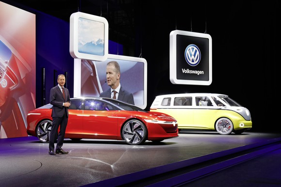 Diess is speaking on stage next to the I.D. Vizzion, a sleek red sedan, and the I.D. Buzz, a yellow and white minivan that recalls the styling of the 1960s VW Microbus.