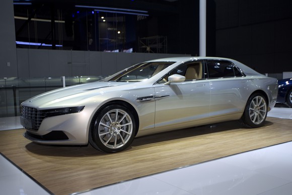 A 2015 Lagonda Taraf, a sleek luxury sedan, in silver on an auto-show display stand.