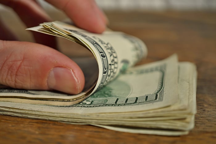 A hand counting a stack of $100 bills.